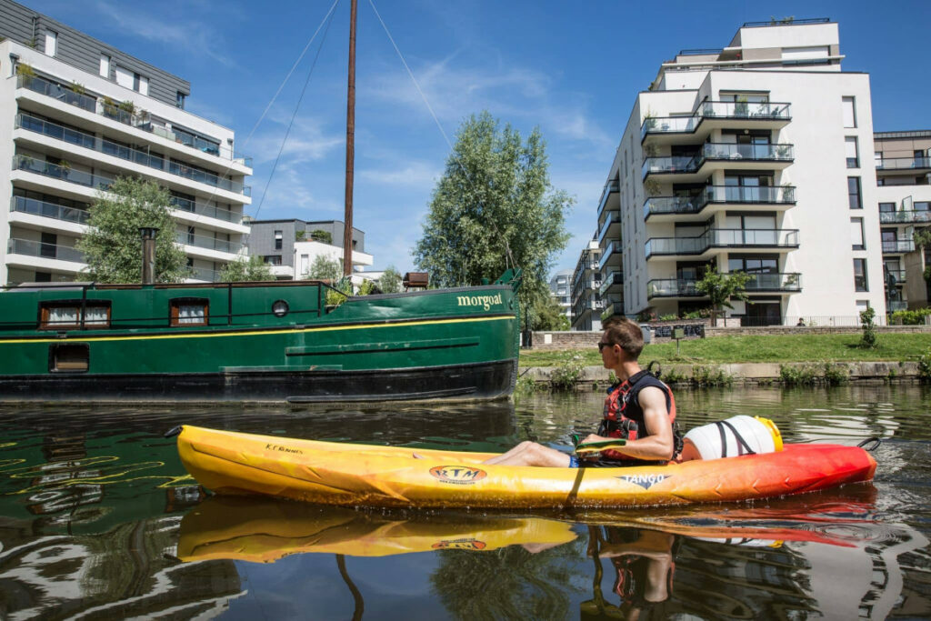 Canoe navigant sur la Vilaine le long du quai Saint-Cyr où des péniches sont amarrées.