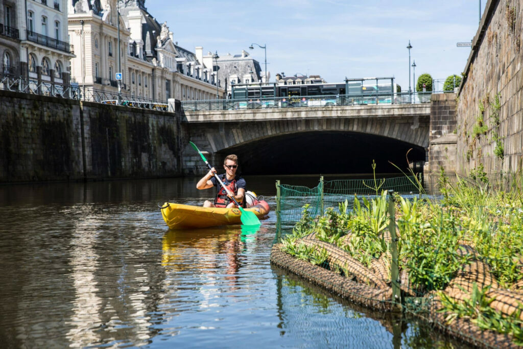 Canoe navigant sur la Vilaine. On y aperçoit la place de la République et le Palais du Commerce.