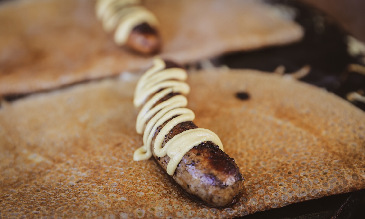 La galette saucisse se savoure nature mais aussi avec de la moutarde.