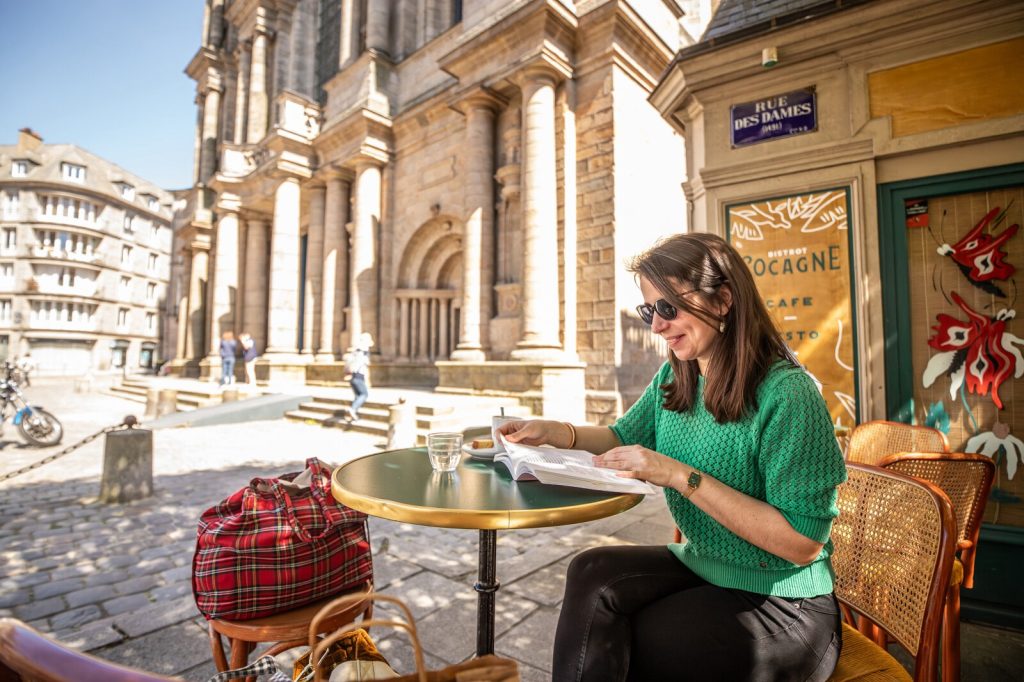 Une femme prend un café en terrasse au bistrot Cocagne face à la cathédrale.