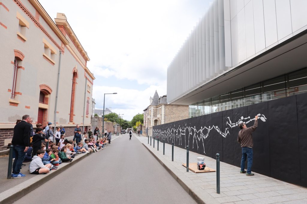 Des élèves assistent à la réalisation de la fresque de l'artiste Jérôme Mesnager, sur le mur de la rue d'Échange, lieu d'expression pour le street-art.