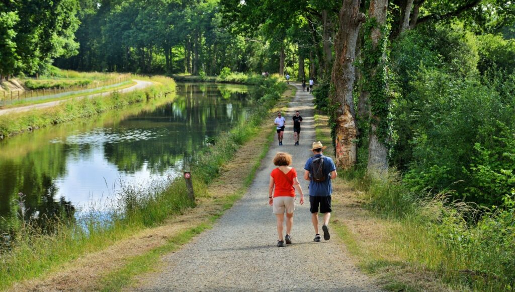 Une couple de randonneurs se promène au bord du canal d'Ille-et-Rance bordé d'arbres à Chevaigné